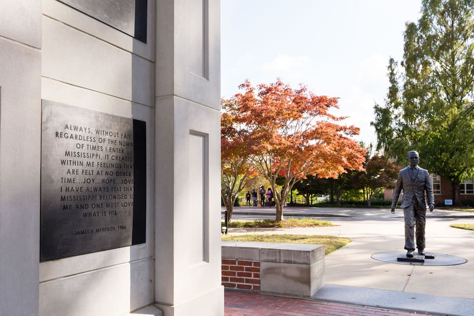 A statue, a plaque with a quote, and autumn-colored trees.