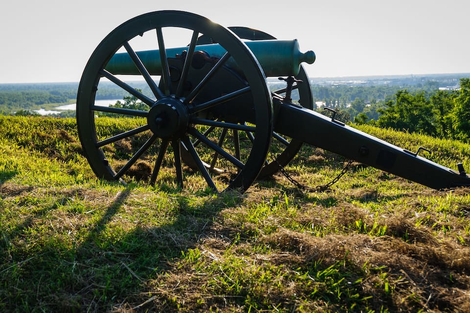 A cannon on a grassy hill overlooking a valley.