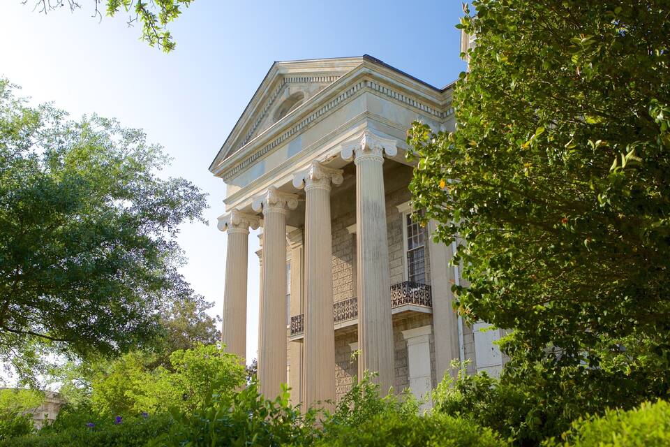 A neoclassical building with columns and a triangular pediment, surrounded by lush green trees.