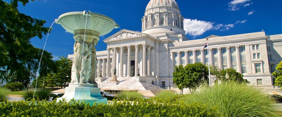 A large neoclassical building with a prominent dome and columns, a fountain, and well-maintained greenery.