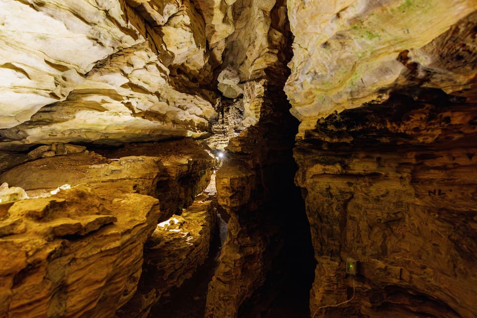 A narrow cave passage with stalactites and stalagmites.