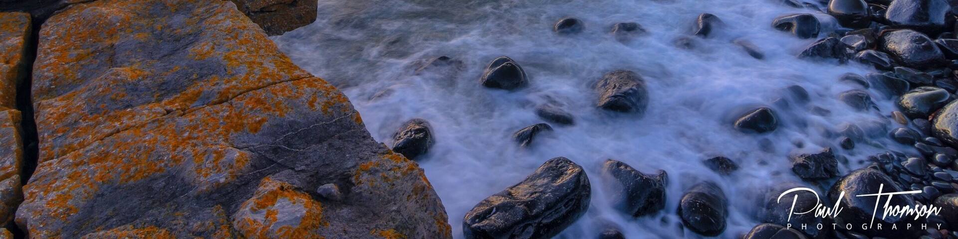 A coastal landscape with a castle on a hill, rocky shoreline, and ocean waves.
