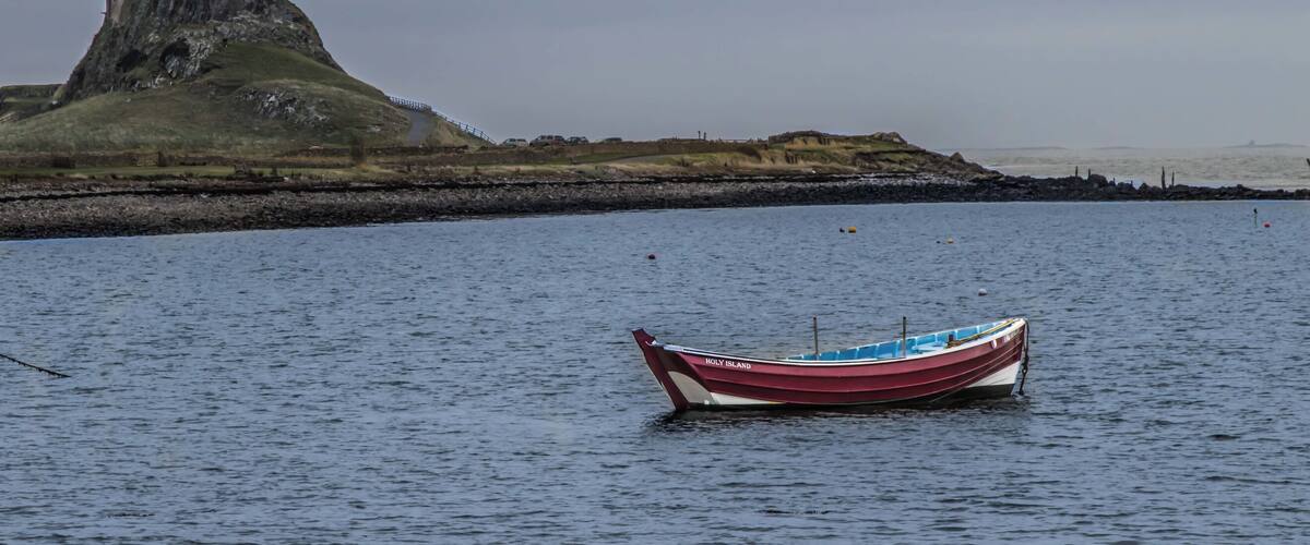 A boat named "ITALY ISLAND" on calm water with a rocky coastline and a castle-like structure in the background.