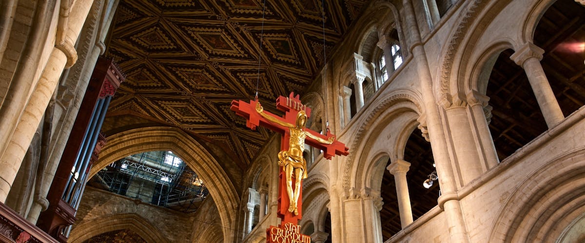 A cathedral interior with a golden crucifix, arched columns, and a patterned ceiling.