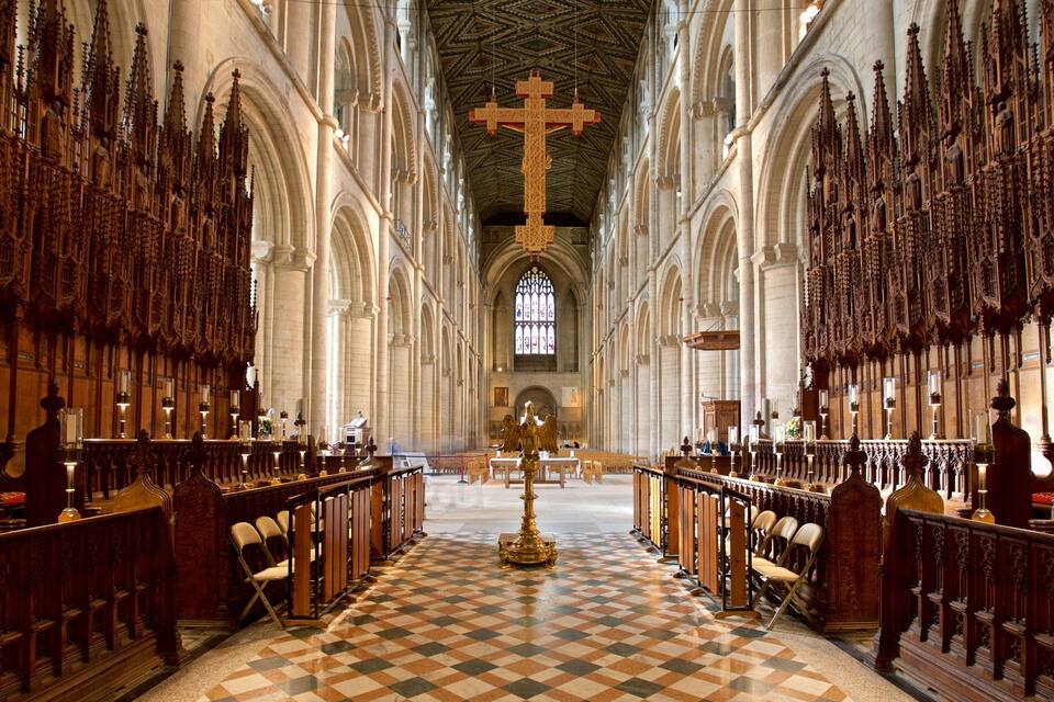 A cathedral interior with high vaulted ceilings, a large central cross, and a checkered floor.