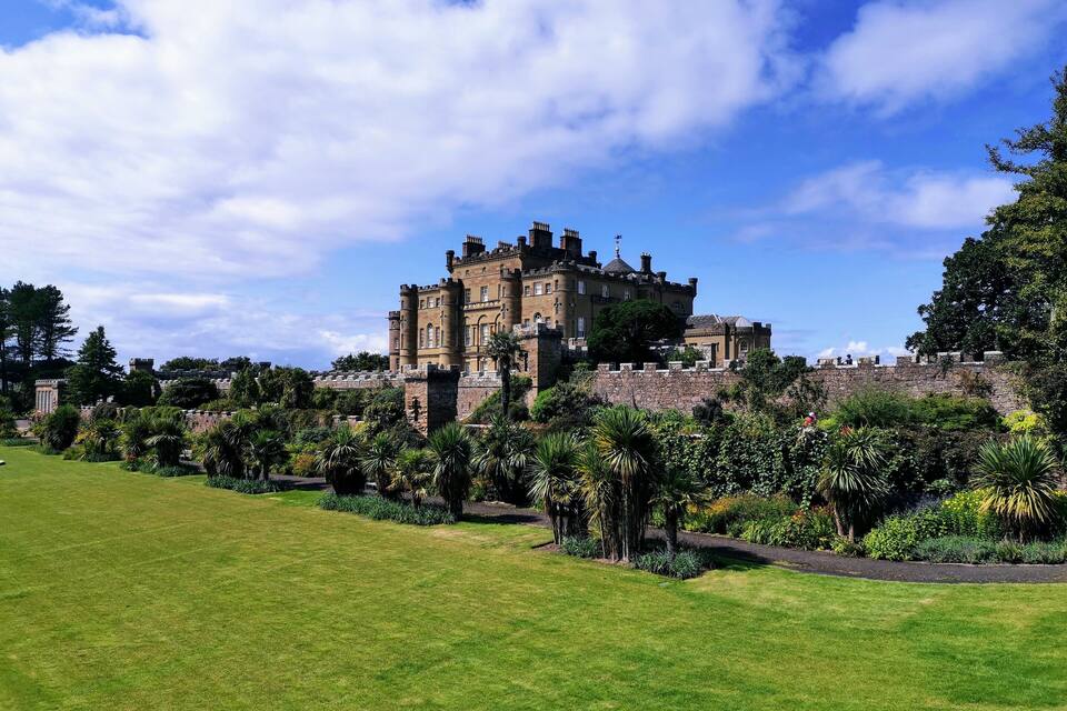 A historic castle surrounded by lush gardens and a clear blue sky.
