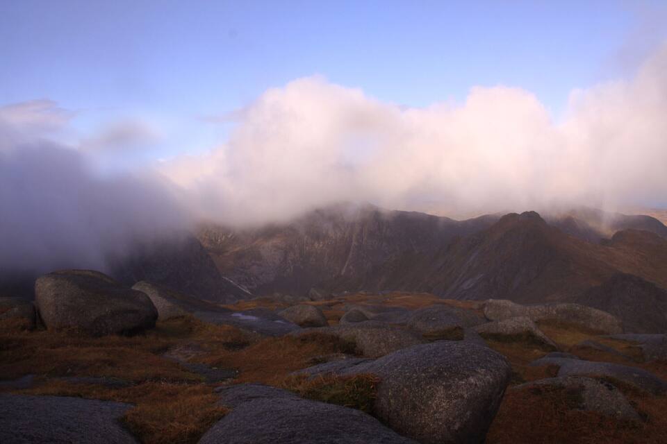 A mountainous landscape with large boulders and grassy terrain under a cloudy sky.