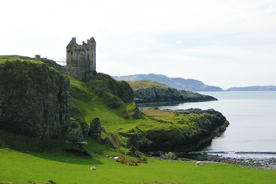 A coastal landscape with a ruined castle on a grassy hill overlooking the sea.