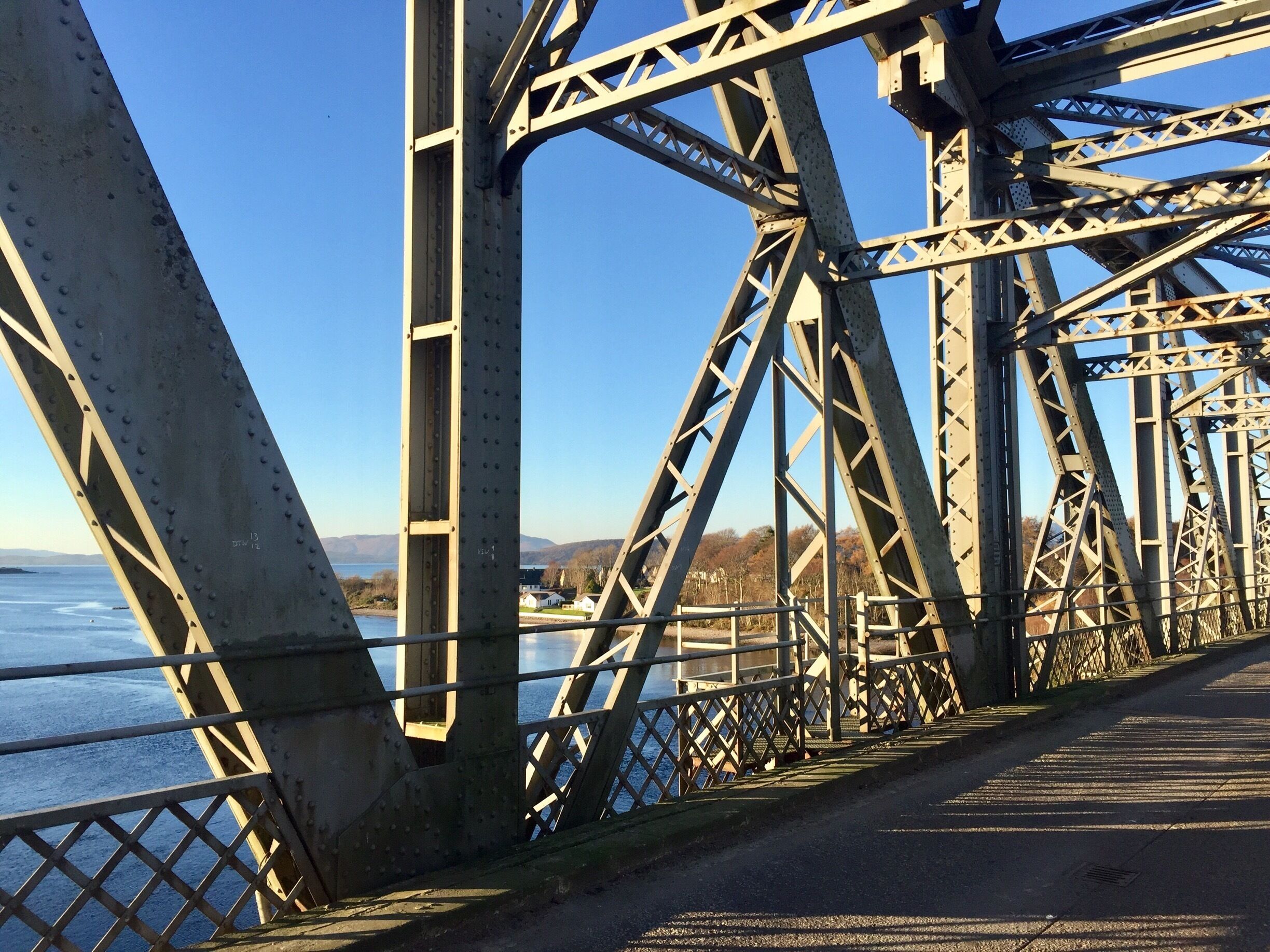 A steel bridge with a clear view of the water below and distant hills.