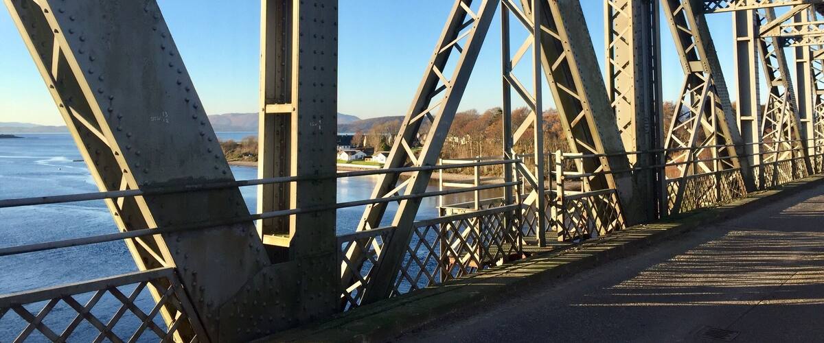 A steel bridge with a clear view of the water below and distant hills.