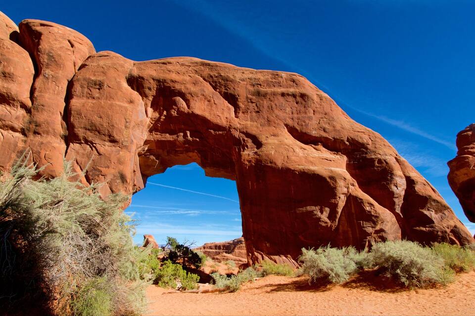 A large red rock arch formation with sparse vegetation around it.
