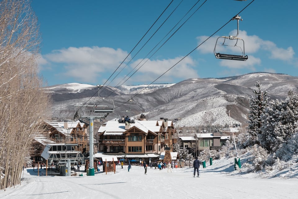 A snow-covered ski resort with wooden buildings, a ski lift, and a mountain backdrop.