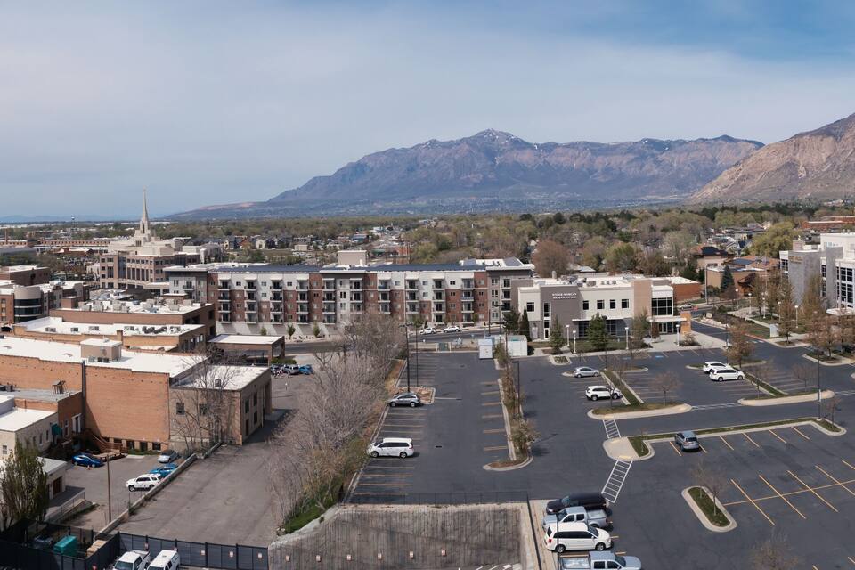 An aerial view of a city with a large parking lot, buildings, and mountains in the background.