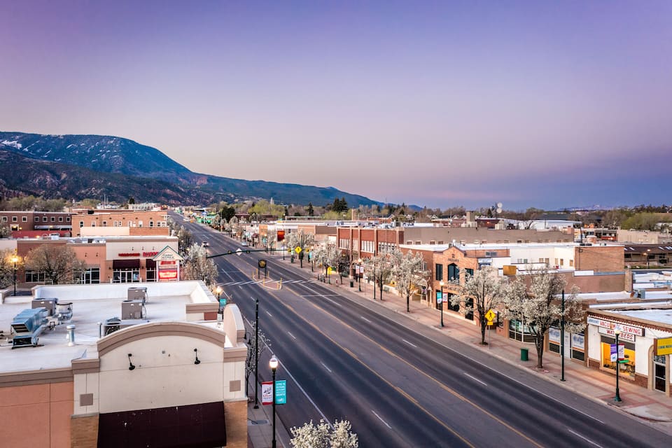 A wide street lined with buildings and trees, with mountains in the background.
