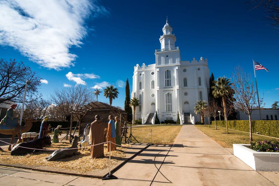 A white church with a bell tower, palm trees, and a flag.