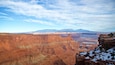 A canyon with layered rock formations, a distant mountain range, and a clear sky.