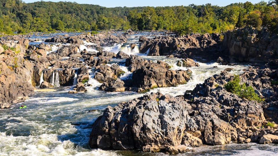 A river with multiple waterfalls surrounded by rocky terrain and dense forest.
