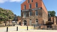 A historic building named "Historic Tredegar" with brick architecture, a large sign, and a paved area with benches and a tree with pink flowers.