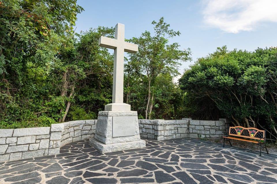A stone cross surrounded by greenery and a stone bench.