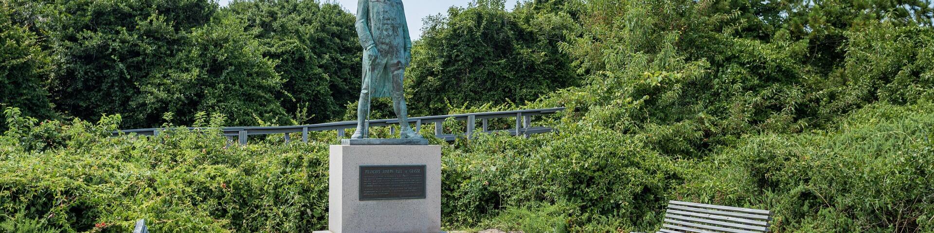 A statue of a man on a pedestal in a park with benches and lush greenery.