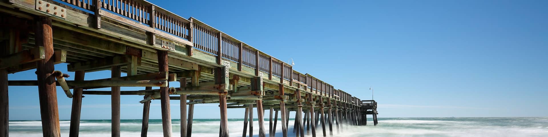 A wooden pier extending into the ocean with waves lapping at its base.