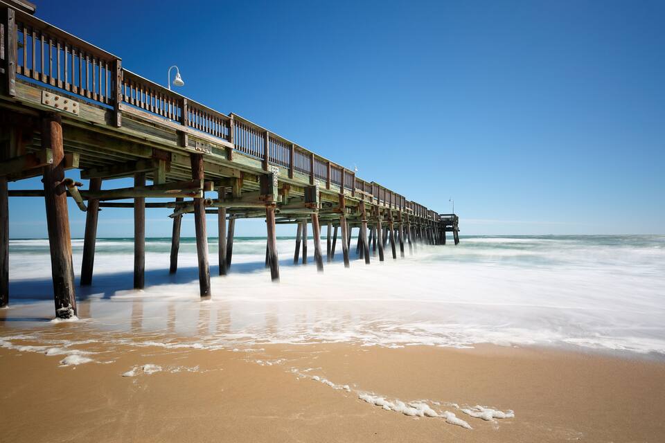 Un muelle de madera que se adentra en el océano, con olas rompiendo a su alrededor.