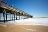A wooden pier extending into the ocean with waves lapping at its base.
