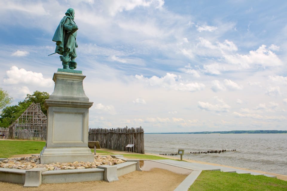 A statue on a pedestal by a lake with a wooden fence and a grassy area in the foreground.