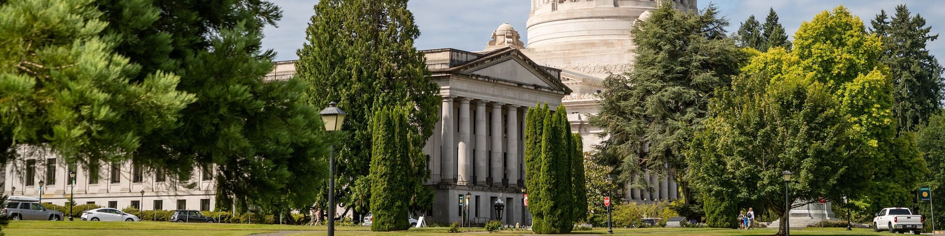 A large government building with a prominent dome and columns, surrounded by well-maintained lawns and trees.