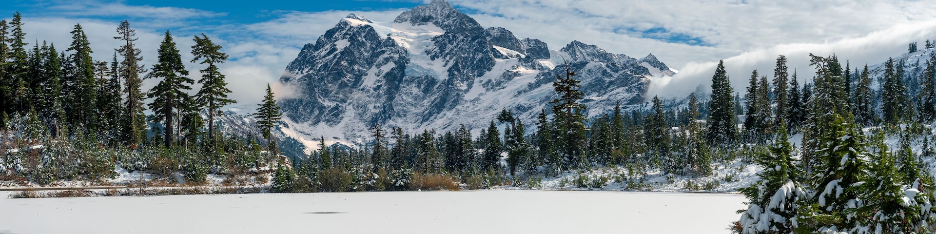 Un lago cubierto de nieve, rodeado de frondosos árboles perennes y una cordillera nevada.