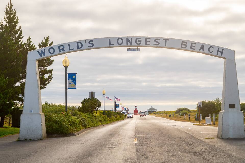 World's Longest Beach sign, a speed limit sign, and a street with cars.