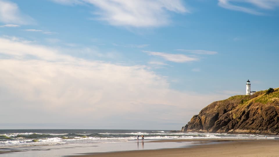 A beach with waves, a lighthouse, and rocky cliffs.