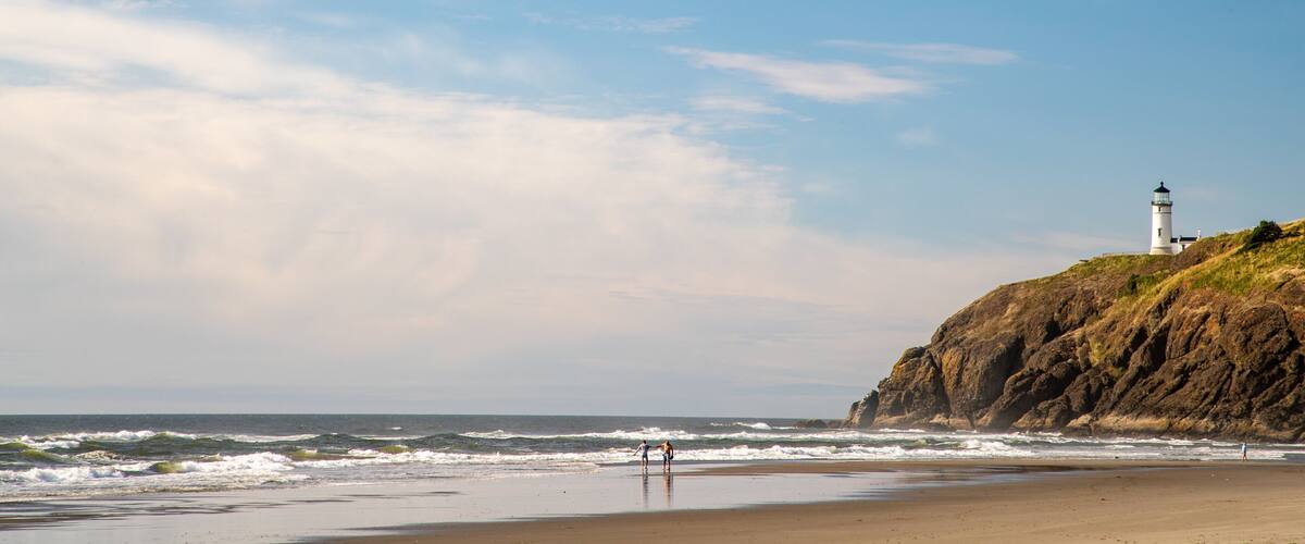 A beach with waves, a lighthouse, and rocky cliffs.