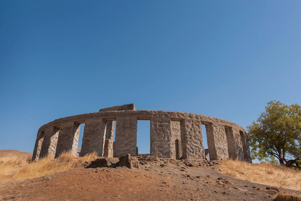 An ancient stone structure with columns, surrounded by dry grass and a clear blue sky.