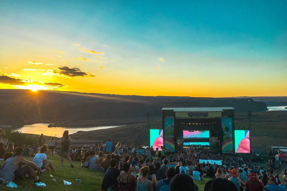 Un atardecer sobre un valle, con una multitud observando un escenario con pantallas grandes.