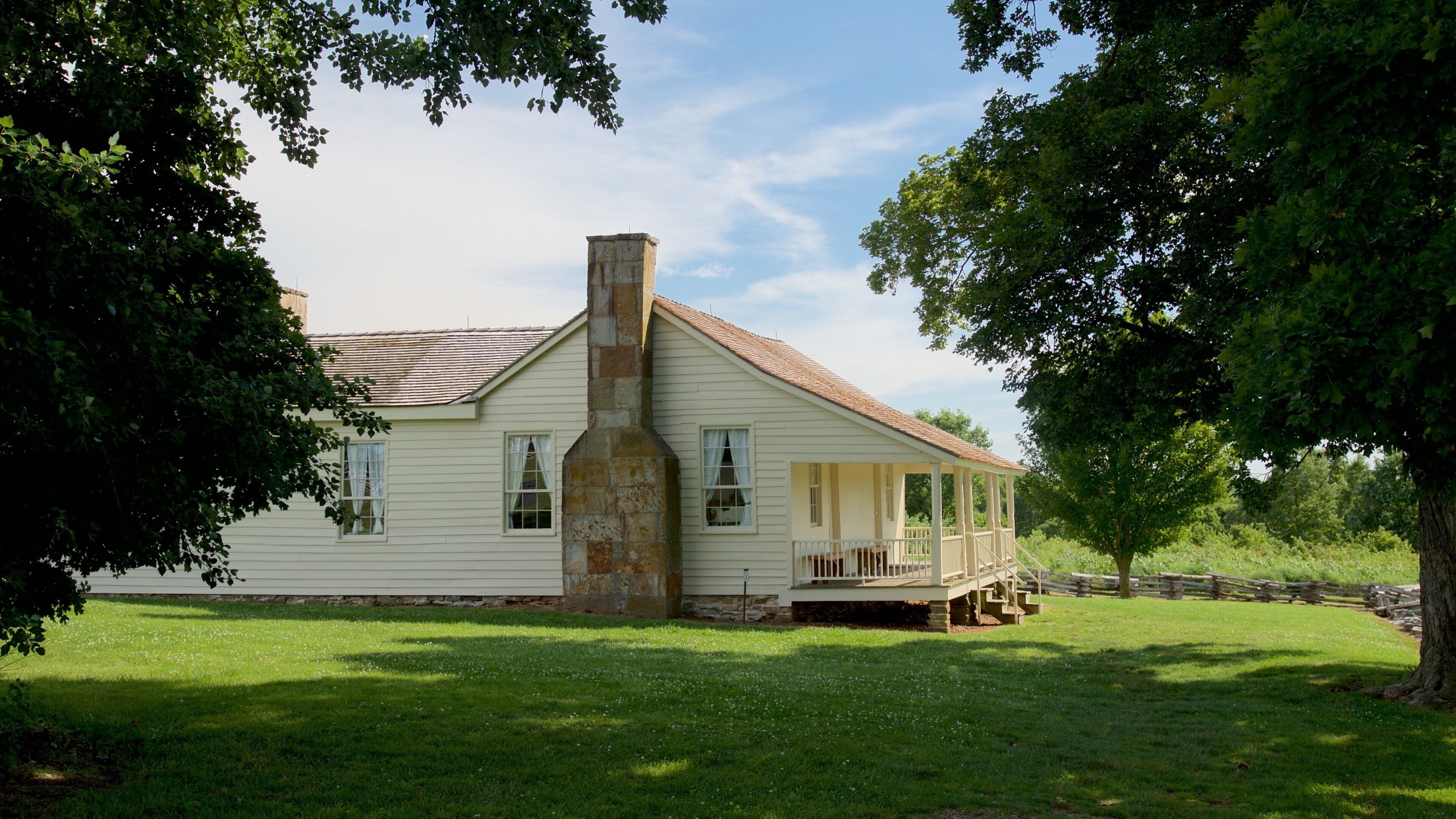 A white colonial-style house with a chimney, surrounded by lush green trees and a well-maintained lawn.