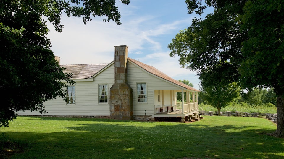 A white colonial-style house with a chimney, surrounded by lush green trees and a well-maintained lawn.
