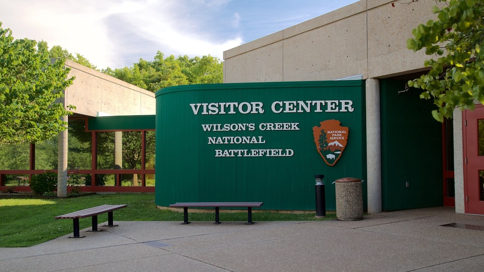 A visitor center with a green sign, a bench, and a trash can.
