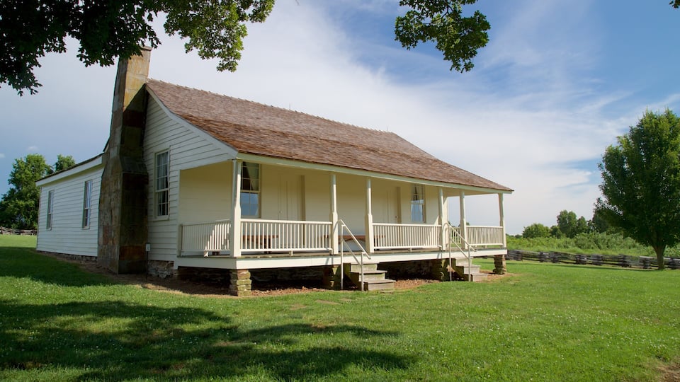 A white wooden house with a porch, surrounded by a grassy field and trees.