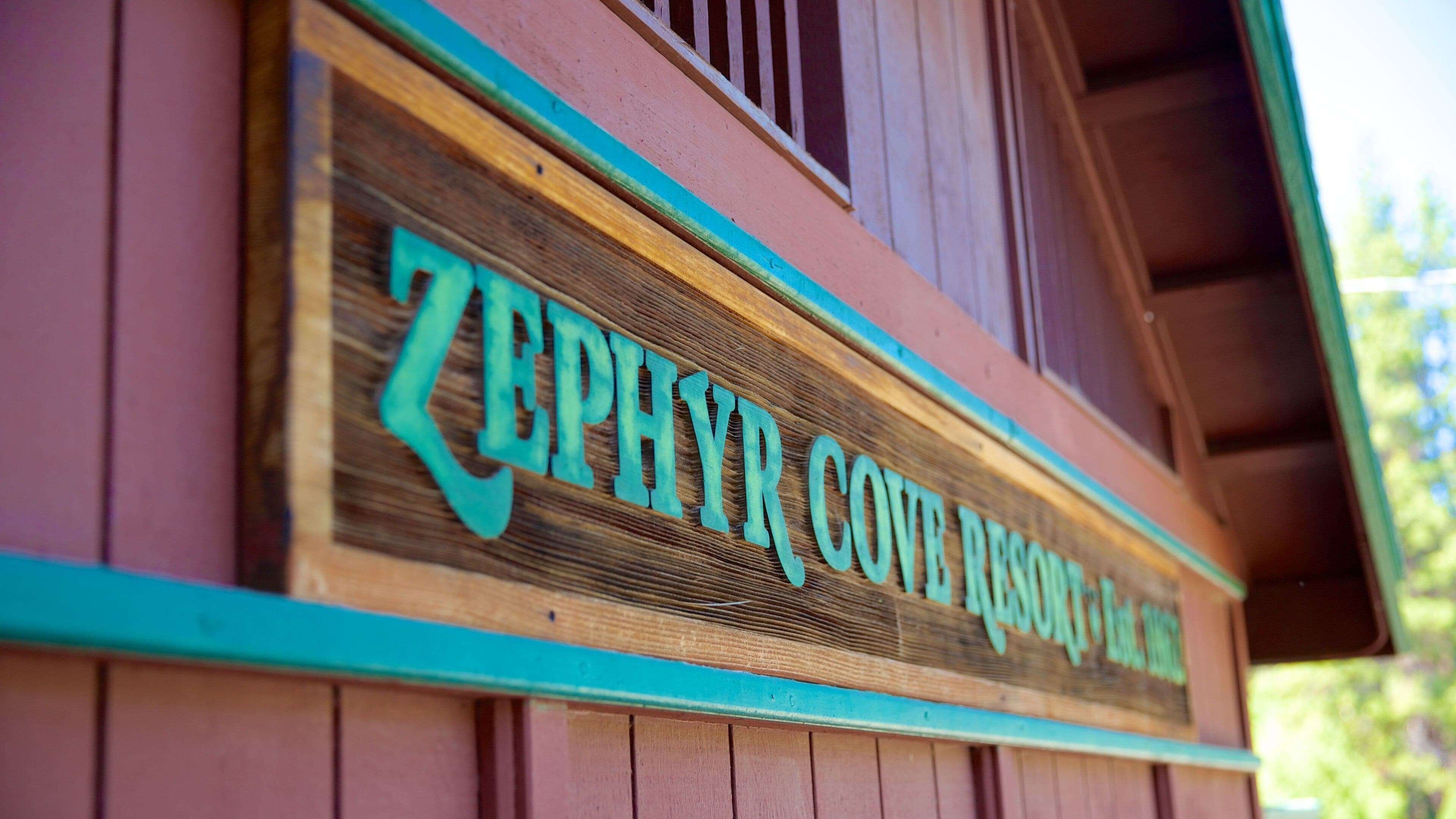 A wooden sign with turquoise letters spelling "ZEPHYR COVE RESORT" on a building.