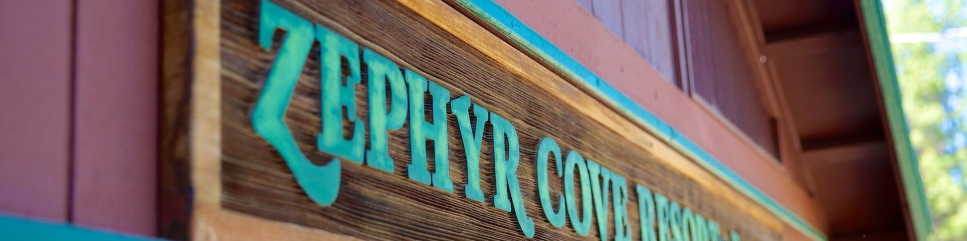 Une enseigne en bois, avec des lettres turquoise, indiquant « ZEPHYR COVE RESORT », est fixée à un bâtiment.