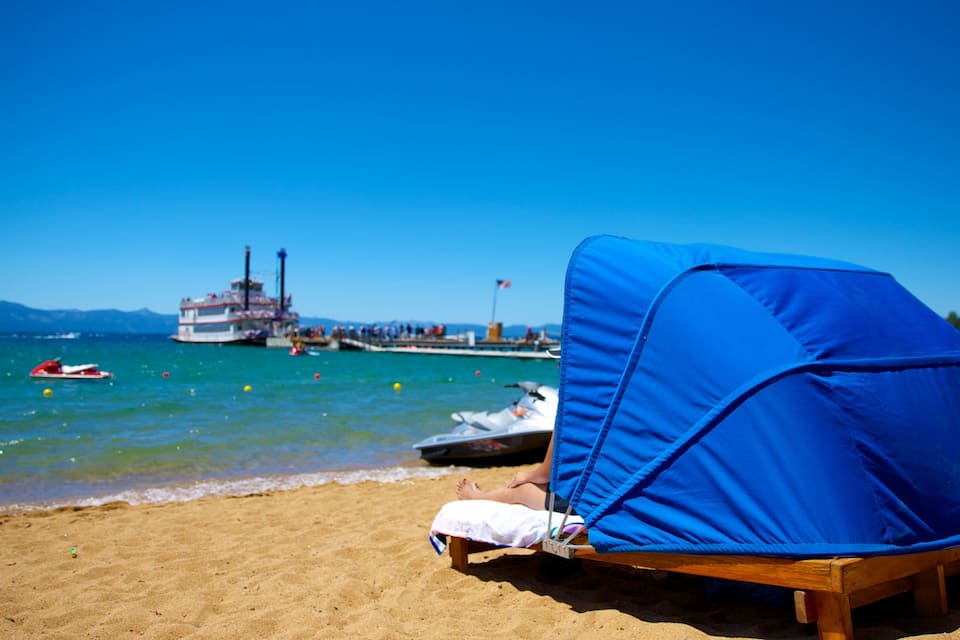 A beach with a blue canopy, a boat, and a pier in the background.
