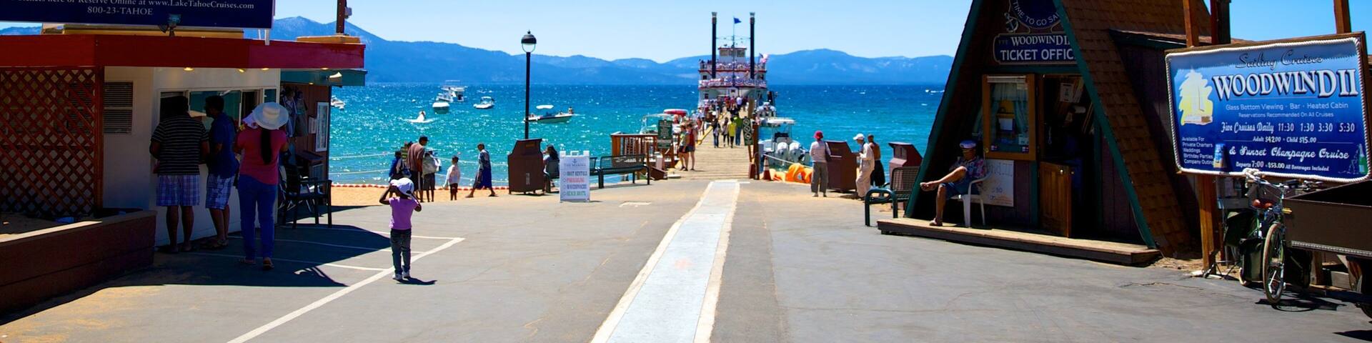A pier with ticket booths for MS Dixie II and Woodwind II cruises, boats in the water, and mountains in the background.