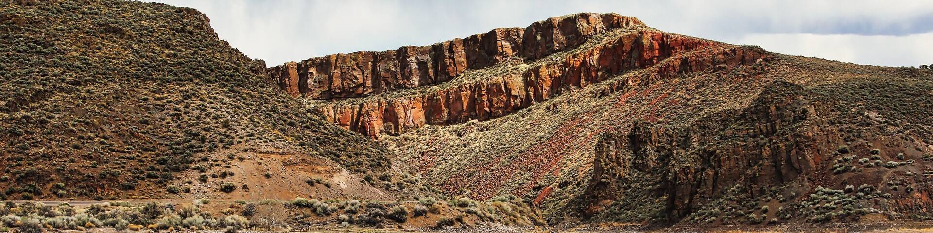 A rugged desert landscape with a dirt road, rocky cliffs, and sparse vegetation.