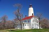 A white lighthouse with a red roof, surrounded by trees with pink blossoms.