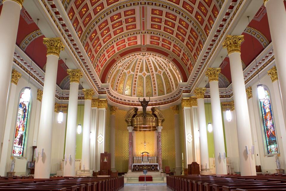 A church interior with a high, ornate ceiling, stained glass windows, and rows of pews.