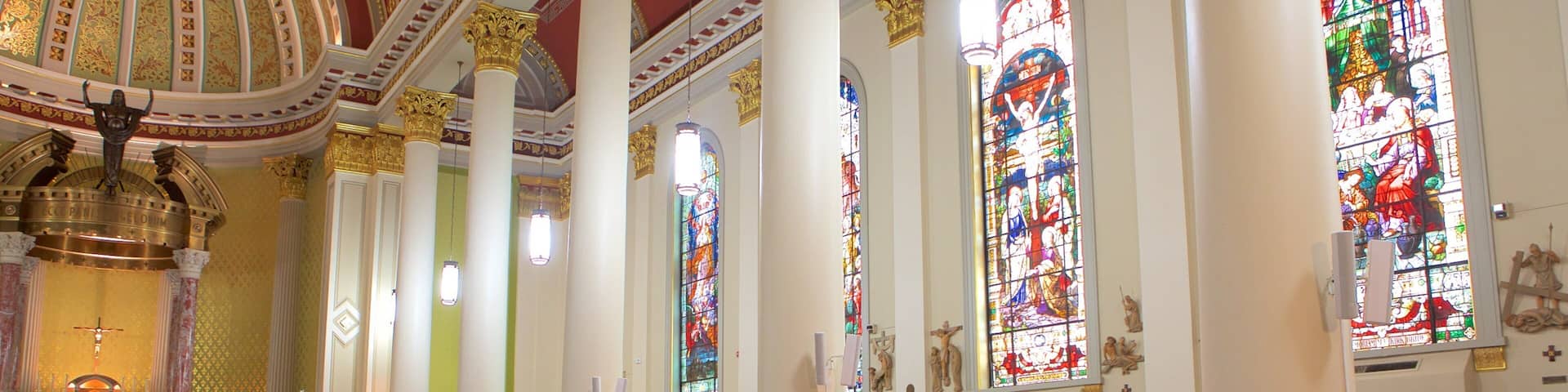 A church interior with rows of pews, stained glass windows, and a large dome ceiling.