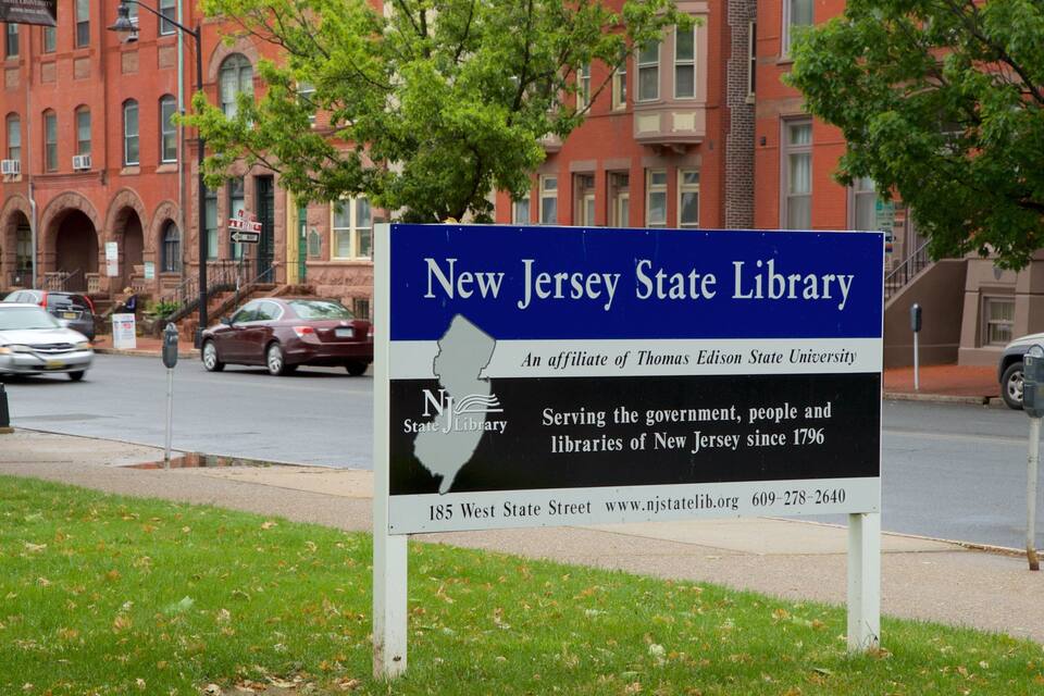 Een bord voor de New Jersey State Library, met een rode bakstenen gebouw op de achtergrond.