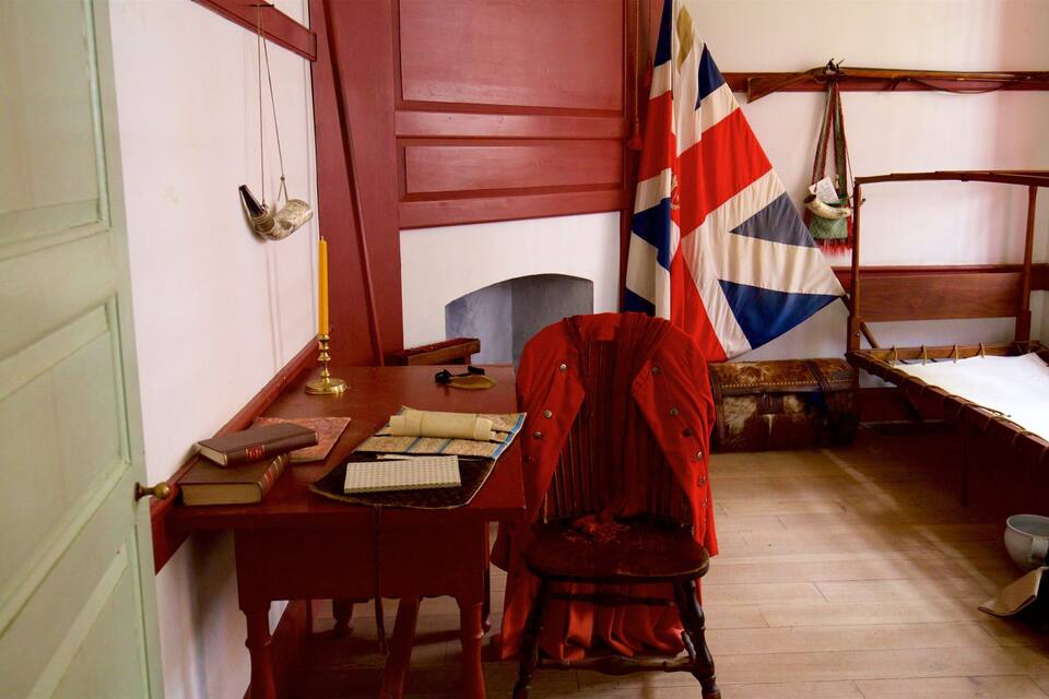 Een kamer met een houten bureau, een stoel, een bed, een vlag en een koffer.