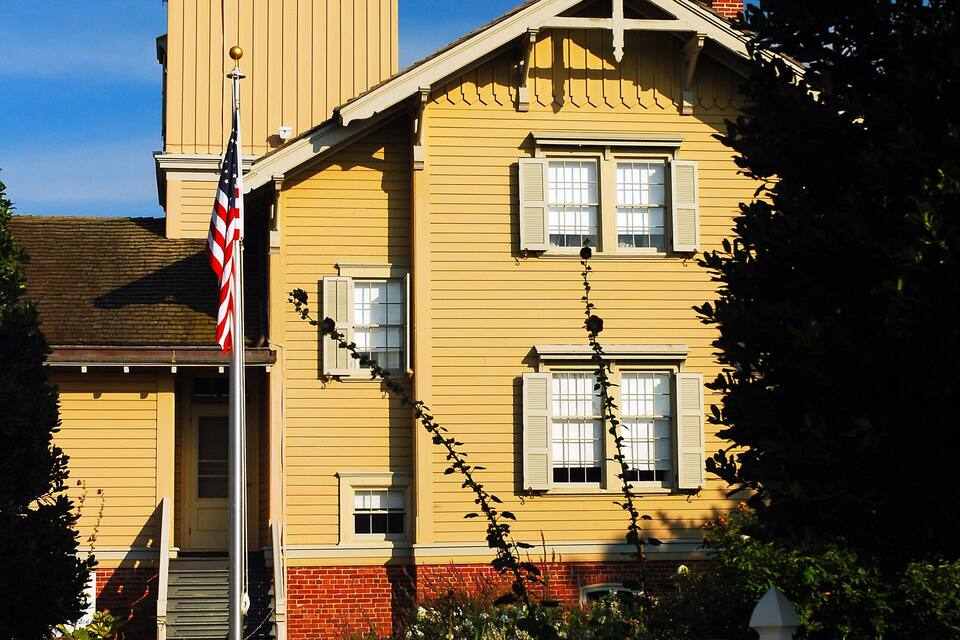 Un edificio giallo con una torre, un recinto di legno bianco e una bandiera americana.